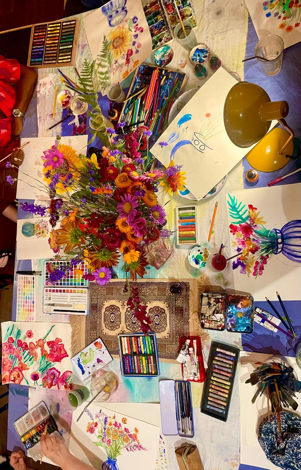 Vue du dessus d'un atelier, un bouquet au milieu des pastels et des dessins.