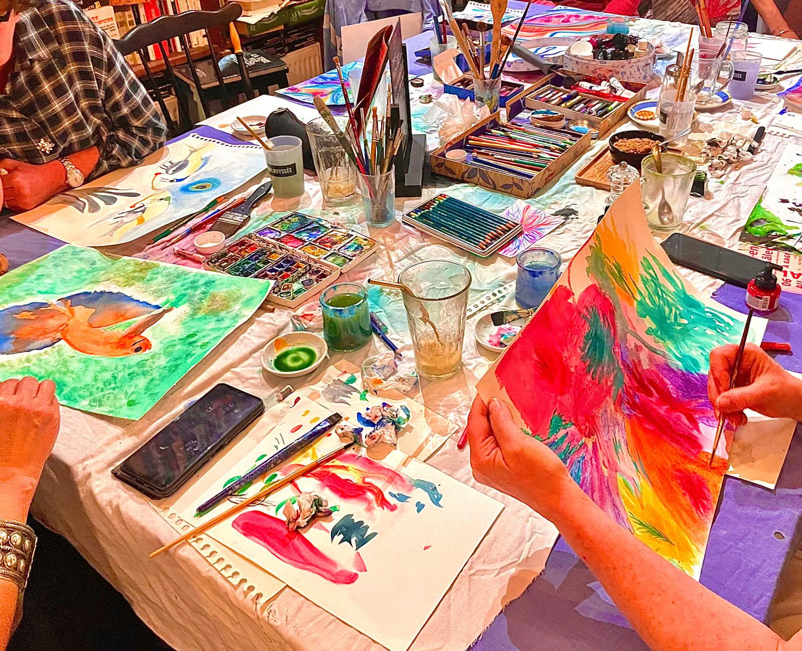 Participants en pleine création, pinceaux, pastels et aquarelles sur la table.