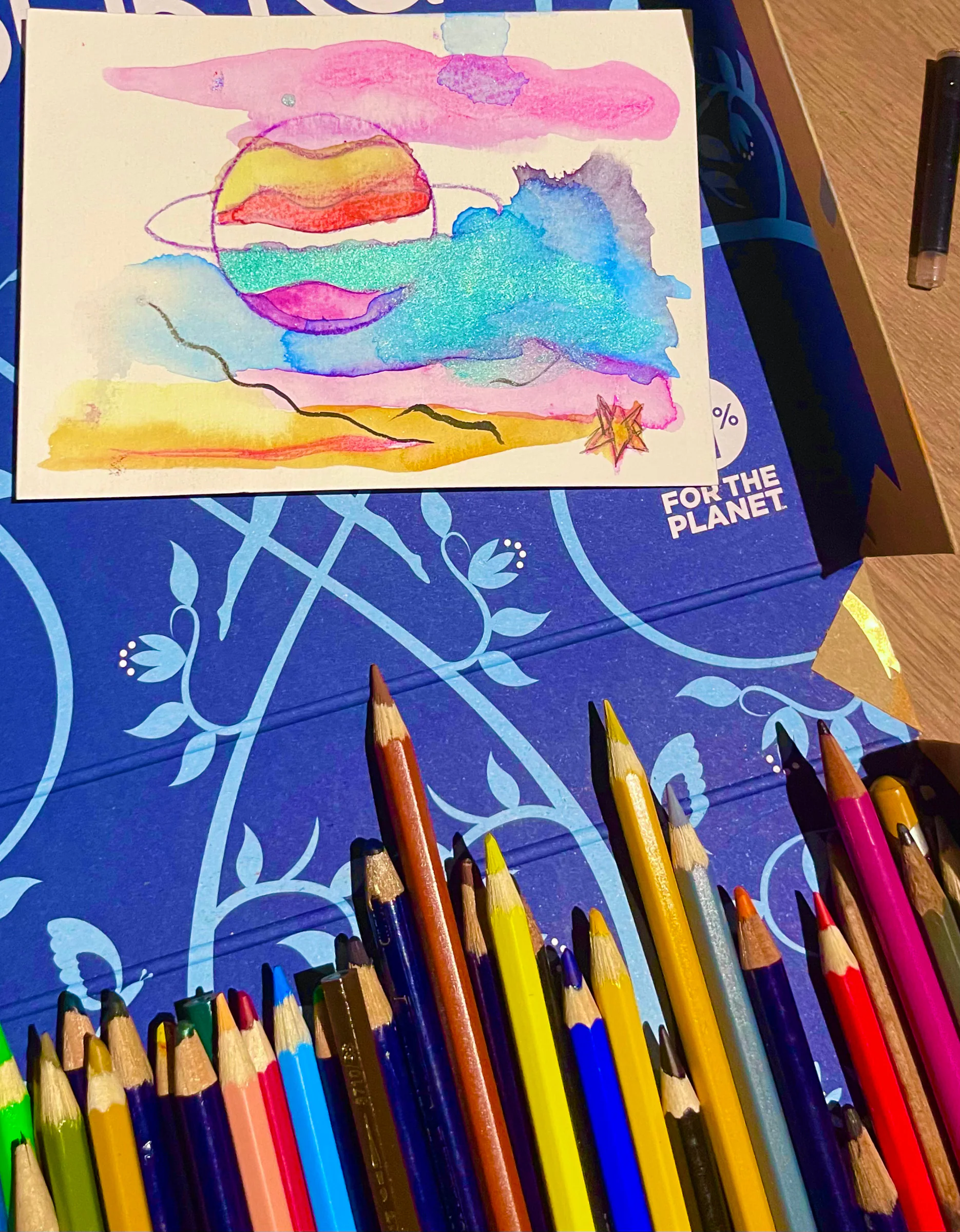 Une aquarelle de planète colorée au-dessus de crayons de couleur.