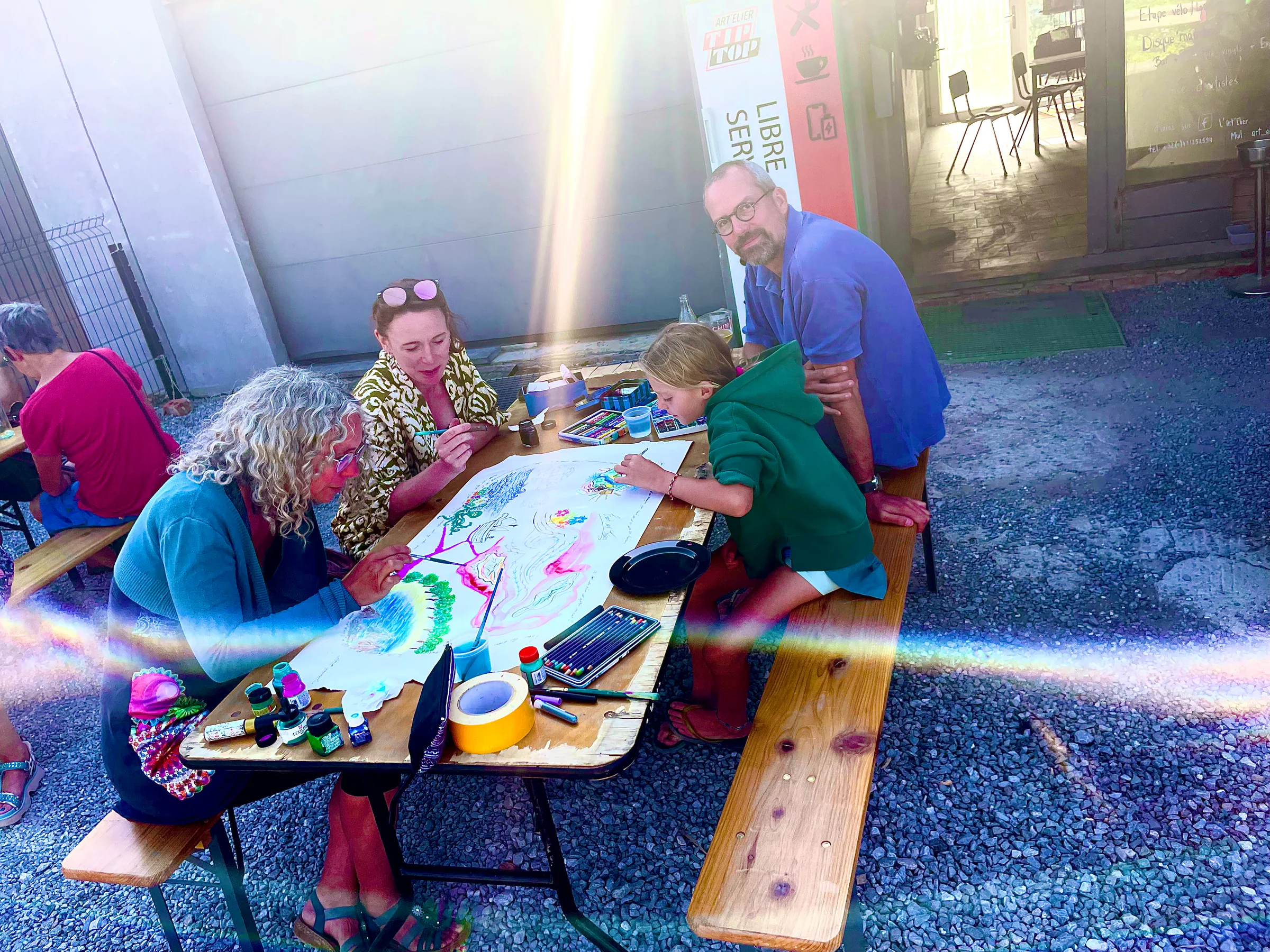 Atelier en plein air, un groupe dessine ensemble autour d'une grande feuille.
