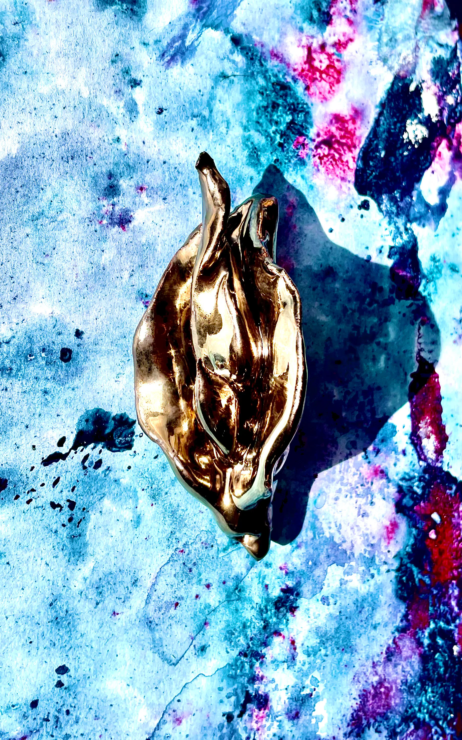 Forme dorée en relief posée sur un fond marbré bleu, blanc et rose.