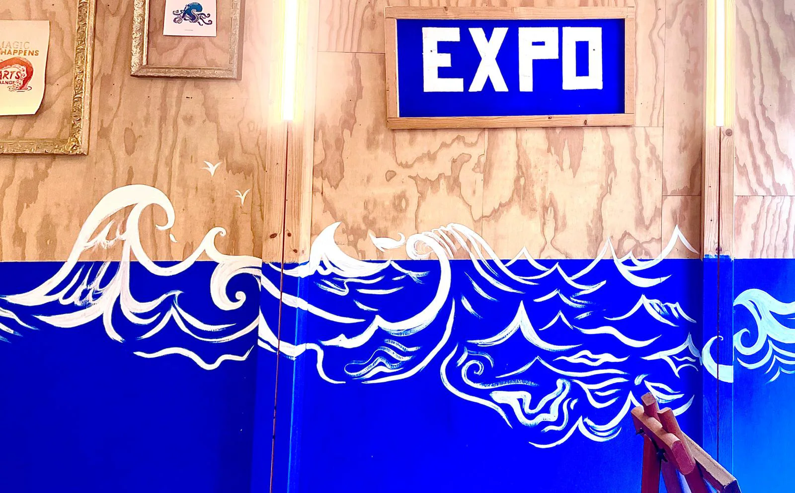 Vagues blanches peintes sur un mur bleu, sous l'enseigne « Expo » de l'Art'elier.