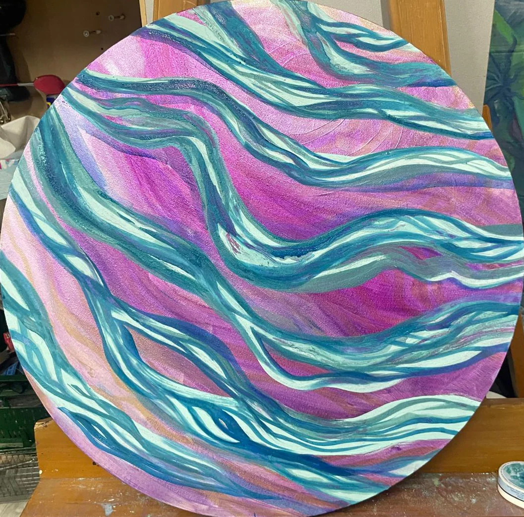 Toile ronde couverte de vagues roses, turquoise et blanches.