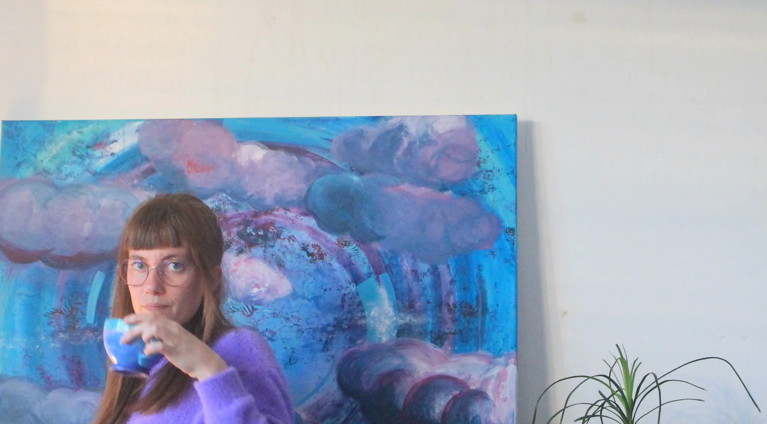 Nina Manon boit un thé devant sa toile aux nuages mauves.